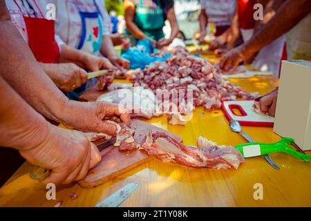 Blick auf Senioren, ältere Menschen, Rentner, Männer und Frauen stehen und schneiden frisches rohes Fleisch auf Holzbrettern mit Messern A in kleinere Stücke Stockfoto