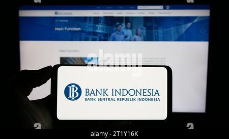 Person, die ein Mobiltelefon mit dem Logo des indonesischen Finanzinstituts Bank Indonesia (BI) vor der Business-Webseite hält. Schwerpunkt auf dem Display des Telefons. Stockfoto