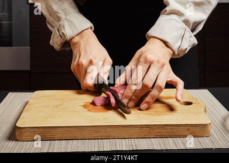 Unerkennbare Frau, die rohes Rindfleischfilet auf Schneidebrett schneidet Stockfoto