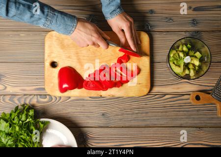 Draufsicht auf weibliche Hände, die roten Paprika mit Küchenmesser schneiden Stockfoto