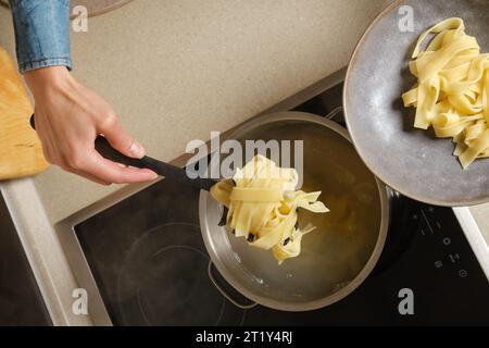 Draufsicht der weiblichen Hand, die gekochte Fettuccin-Pasta aus dem Topf nimmt Stockfoto