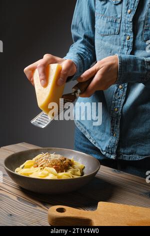 Eine unbekannte Frau reißt Parmesankäse in Pasta Stockfoto