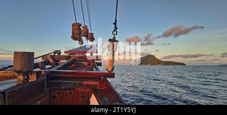 Panoramablick auf den Bug eines Segelbootes, das zu einer abgelegenen und grünen Insel in einem tropischen Meer führt Stockfoto