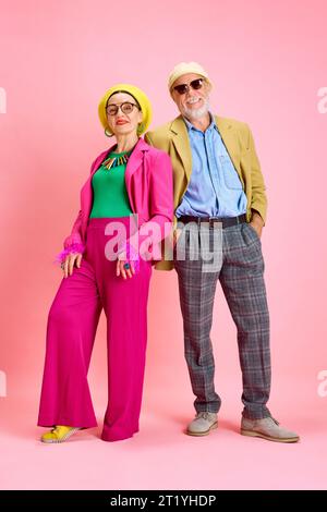 Porträt des schönen älteren Ehepaares, eleganten Mannes und der Frau in stilvoller Kleidung, die vor rosa Hintergrund stehen Stockfoto