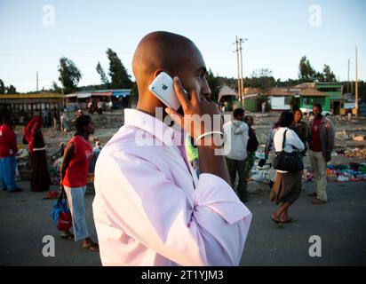 Ein junger Mann läuft eine Straße in Äthiopien entlang, während er sein Handy benutzt. Stockfoto