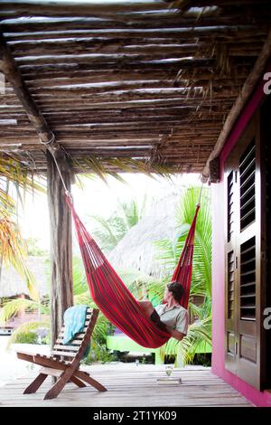 Ein Mann sitzt in seiner Hängematte auf der Veranda seiner Cabana. Stockfoto