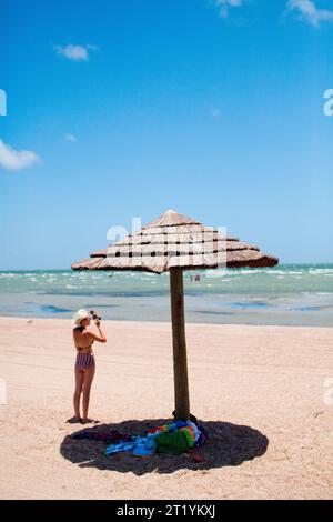 Eine Frau steht an einem leeren Strand neben einem Sonnenschirm. Stockfoto