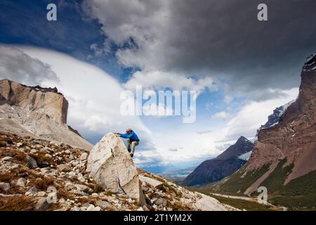 Ein Mann klettert auf einen Felsen mit Blick auf ein dramatisches Tal darunter. Stockfoto