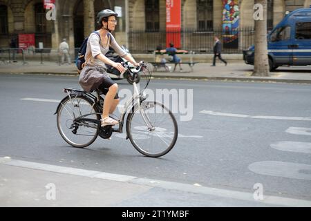 Eine weibliche Fahrradpendlerin in Radshorts unter einem braunen Rock, die einen Fahrradhelm trägt, radelt abends in Paris auf dem Boulevard du Palais entlang Stockfoto