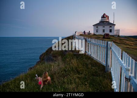 Ein junges Mädchen sitzt am Rande einer Klippe in der Nähe eines Leuchtturms am Cape Spear, Neufundland, Kanada. Stockfoto