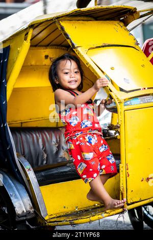 Ein süßes philippinisches Mädchen spielt mit ihrem Vater Dreirad, Pedicab oder Rikscha in Ermita, Manila, Philippinen. Stockfoto