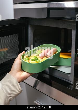 Das Mädchen legt das Essen in die Lunchbox, um sich in der Mikrowelle aufzuwärmen Stockfoto