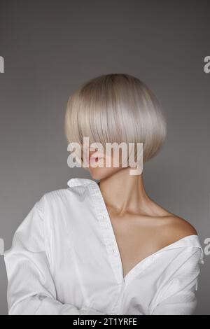 Blonde Frau mit kurzen gefärbten Haaren, kurzen Haarschnitt. Haarwurzelpflege, Frau im Hemdmodeporträt Stockfoto