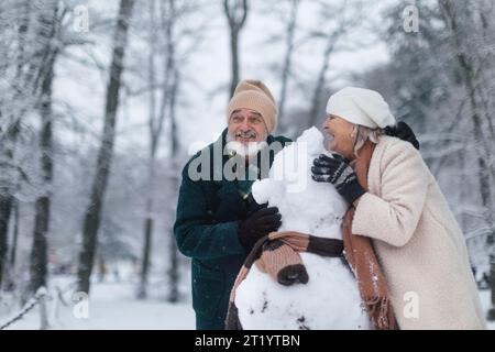 Elegantes Senior Pärchen, das Schneemänner an kalten Wintertagen baut. Älteres Ehepaar verbringt Winterurlaub in den Bergen. Winterliche Landschaft. Stockfoto