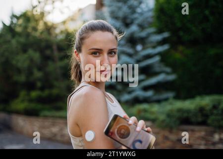 Frau mit Diabetes, die ihr Smartphone vor dem Training mit dem kontinuierlichen Blutzuckersensor verbindet. Diabetikerin überprüft ihren Blutzuckerspiegel Stockfoto