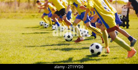 Fußball-Juniorspieler im Trainingskurs. Jungs üben Fußball auf einem Rasenfeld. Eine Gruppe von Schulkindern, die laufen und Fußballbälle antreten Stockfoto