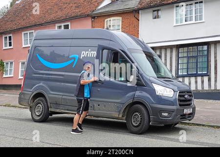 Fahrer mit Prime Delivery, der zum Ford Amazon Van zurückkehrt, um die Paketzustellung zum Dorfwohnhaus mit seitlichem Markenlogo England UK abzuschließen Stockfoto