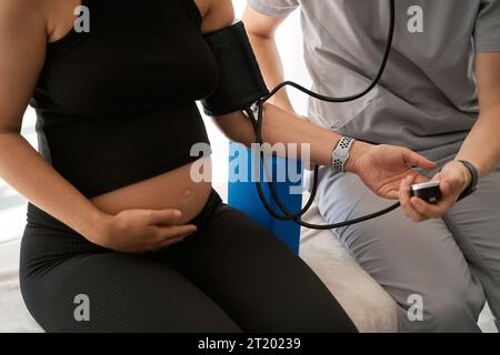 Der Mann in Uniform misst den Blutdruck der schwangeren Frau Stockfoto