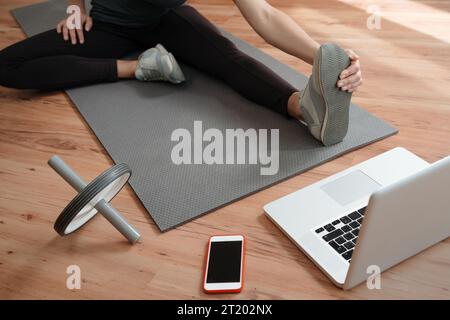 Junge Frau in Sportbekleidung, die Online-Yoga oder Workout-Lektion auf dem Laptop ansieht und Übungen auf dem Boden macht, während sie während der Coronavirus-Pandemie zu Hause bleibt. Fitness- und Wellnesskonzept Stockfoto