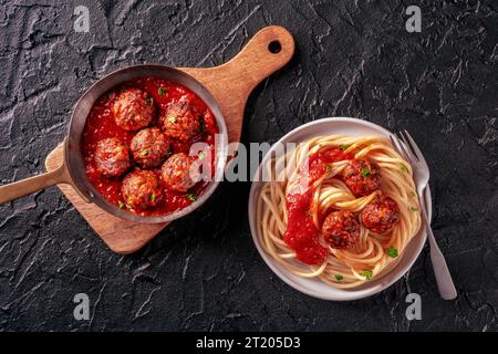 Fleischbällchen. Rindfleischbällchen, italienisches Gericht, oben flach in einer Pfanne und mit einem Teller Spaghetti Nudeln, auf schwarzem Hintergrund Stockfoto