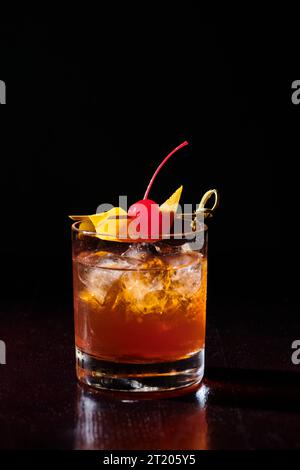 Eiskalte intensive negroni garniert mit Cocktailkirsche auf schwarzem Hintergrund, Konzept Stockfoto