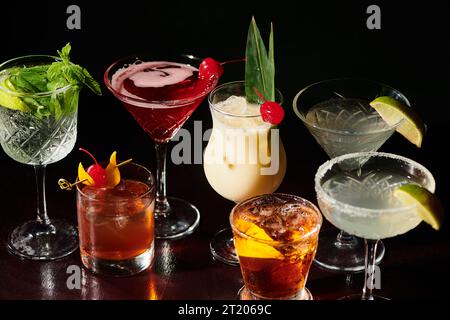 Köstliches erfrischendes Set ästhetischer Cocktails mit Garnierungen vor schwarzem Hintergrund, Konzept Stockfoto