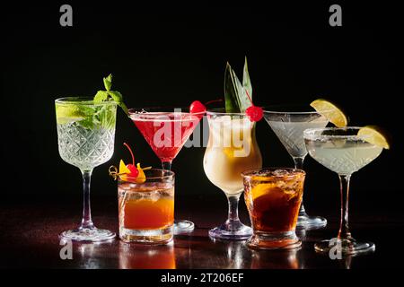 Set aus verschiedenen raffinierten Cocktails mit frischen Garnituren auf schwarzem Hintergrund, Konzept Stockfoto