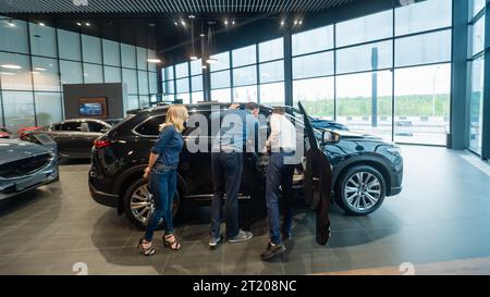 Der Verkäufer demonstriert den Käufern das Fahrzeuginnere. Ein weißes Paar sucht sich ein Auto aus. Stockfoto