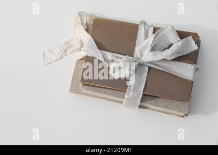 Ein Stapel von drei alten, alten Büchern, gefesselt mit beigefarbenem Band und Leineneinband. Seidenschleife. Weißer Tischhintergrund, flache Anordnung, Draufsicht. Literatur Stockfoto