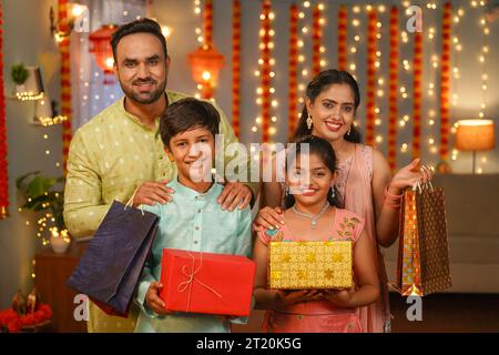 Glückliche indische Familie, die mit Geschenkboxen und Einkaufstaschen steht, indem sie während der diwali-Feier zu Hause die Kamera schaut - Konzept des festlichen Einkaufs Stockfoto