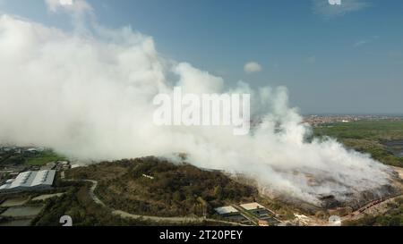 Ein starkes Feuer auf der größten Deponie der Insel Bali. Das Feuer wird von vielen Feuerwehrfahrzeugen und Hubschraubern gelöscht. Eine riesige Spalte von en Stockfoto