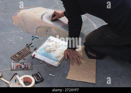 Straßenkünstler, der mit farbigen Kreiden eine Reproduktion eines berühmten Gemäldes auf einem Bürgersteig auf der Straße präsentiert. Stockfoto