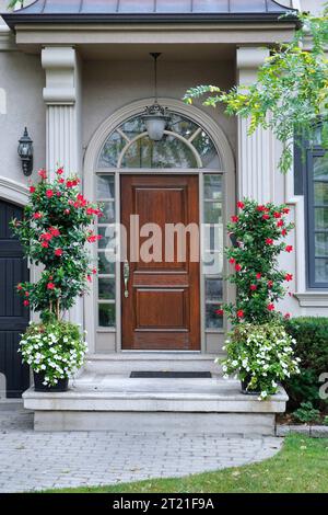 Hauseingang mit eleganter Haustür aus Holz und roten Blumen Stockfoto