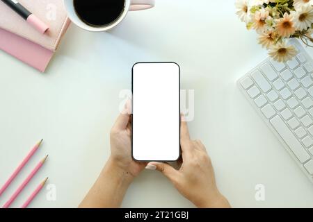Zugeschnittene Aufnahme von Draufsicht von Geschäftsfrauen mit Smartphone-Mockup am weißen Schreibtisch. Mobiltelefon mit leerem Bildschirm für die Montage des Grafikdisplays. Stockfoto