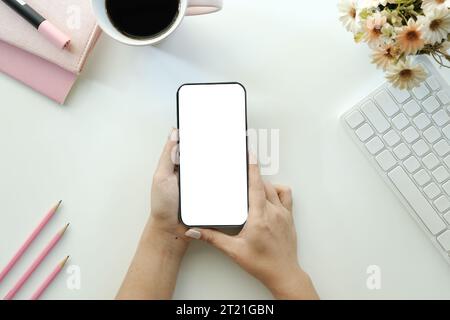 Zugeschnittene Aufnahme von Draufsicht von Geschäftsfrauen mit Smartphone-Mockup am weißen Schreibtisch. Mobiltelefon mit leerem Bildschirm für die Montage des Grafikdisplays. Stockfoto