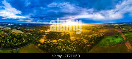 Ein atemberaubender Sonnenuntergang färbt den Himmel in wunderschönen Orange- und Rottönen über einem unbefestigten grünen Feld Stockfoto