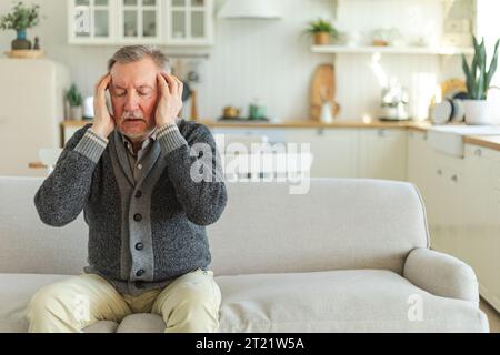 Kopfschmerz. Unglücklicher Mann mittleren Alters mit Kopfschmerz-kranken Reibungstempeln zu Hause. Reifer alter Großvater berührt Tempel unter Stress. Ein Mann, der Schmerzen im Kopf hat Stockfoto