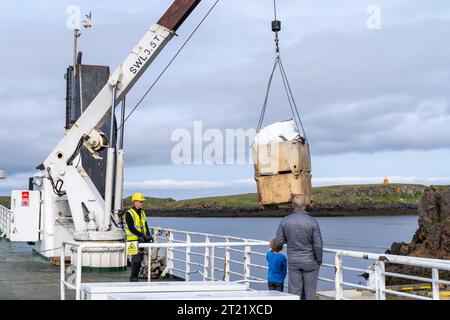 Stykkisholmur, Island - 2. Juli 2023: Angestellter lädt Fracht auf die Fähre Baldur in Island, während ein Vater und Sohn Passagiere beobachten Stockfoto