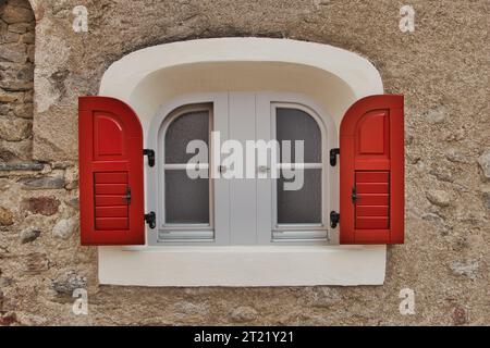 Eine Nahaufnahme eines Fensters mit weißen Wänden und roten Fensterläden Stockfoto