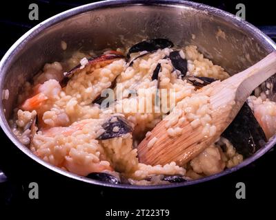 Ein köstliches italienisches Meeresfrüchterisotto mit Safran-Reis in einem Topf mit einem Holzlöffel. Stockfoto