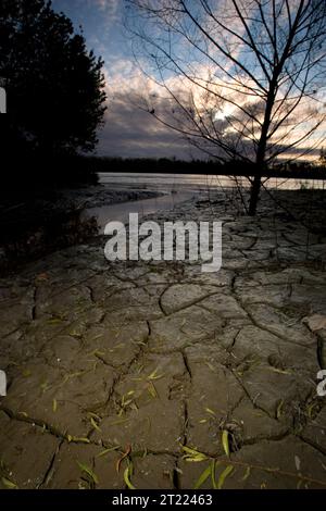 Sonnenuntergang über einer zerrissenen Schlammfläche im Big Muddy National Fish and Wildlife Refuge, Missouri, mit sichtbarem Missouri River im Hintergrund. Stockfoto