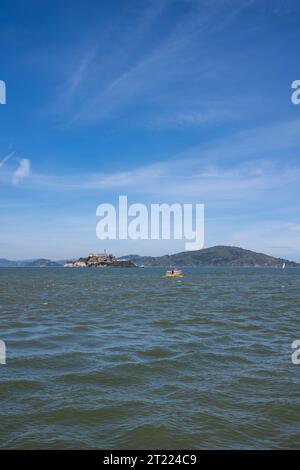 Malerischer Blick auf die Insel Alcatraz mit einem Boot, das auf plätscherndem Meereswasser vor blauem Himmel mit Wolken und Bergen in San Francisco schwimmt Stockfoto