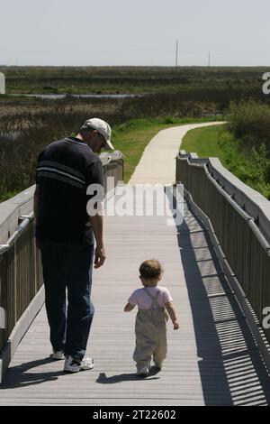 Ein Mann und ein Kleinkind machen einen gemütlichen Spaziergang entlang einer Promenade im Sabine National Wildlife Refuge in Louisiana und genießen die natürliche Schönheit und Tierwelt der Region. Stockfoto