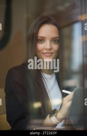 Niedliche junge Frau, die eine Skizze auf einem Tablet-pc zeichnet. Freischaffender Illustrator, der in einem Restaurant arbeitet Stockfoto