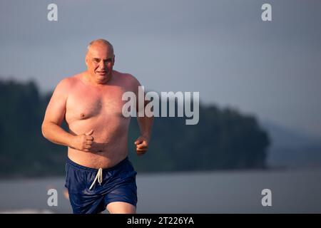 Ein alter Mann mit sportlicher Stärke joggt am Meer entlang. Der Mann geht zum Sport. Stockfoto