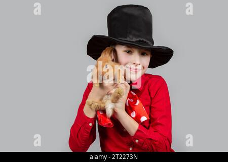 Ein Magier-Junge mit schwarzem Hut hält ein rotes Kaninchen. Stockfoto