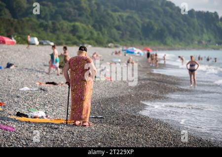 04. August 2022. Georgien, Batumi. Strand. Eine ältere Frau mit einem Stock ruht auf einem felsigen Ufer. Stockfoto
