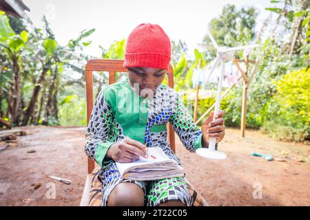 Ein afrikanisches Kind macht Hausaufgaben über erneuerbare Energien und hält eine Miniatur-Windenergieanlage in der Hand. Stockfoto