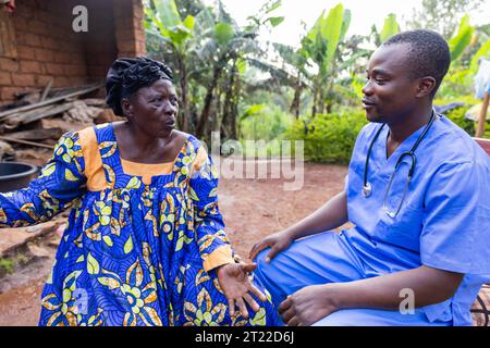 Ein Arzt spricht mit seinem älteren Patienten während eines Hausbesuchs in einem afrikanischen Dorf. Stockfoto