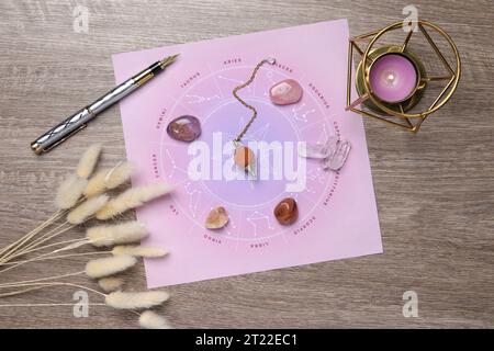 Astrologie-Vorhersage. Zodiac-Rad, Edelsteine, Pendel und brennende Kerze auf Holztisch, flache Ladefläche Stockfoto